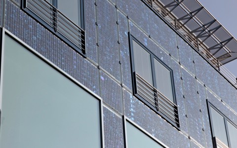 Fassade eines modernen Gebäudes mit integrierten Solarpaneelen und grossen Fenstern.