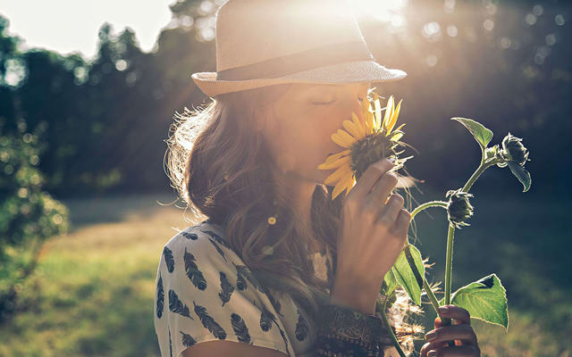 Donna annusa un girasole – simbolo di un’economia energetica rinnovabile e vicina alla natura.