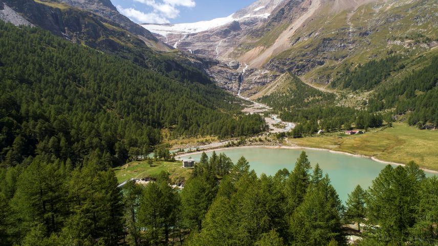 Blick auf das Kraftwerk Palü mit See, Wasserfällen und Gletscher im Hintergrund inmitten alpiner Landschaft.